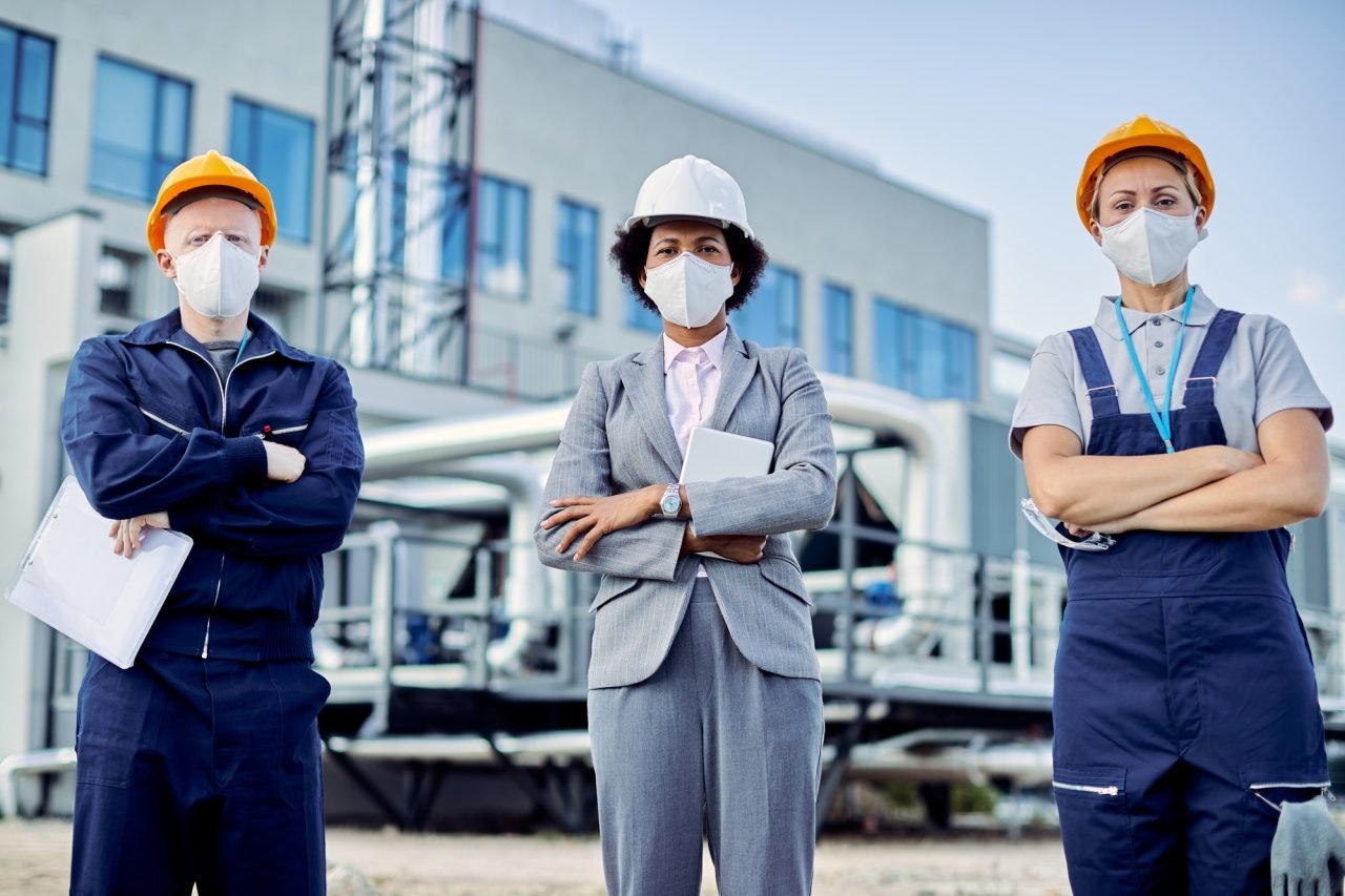 Team of confident civil engineers with protective face masks and construction site.